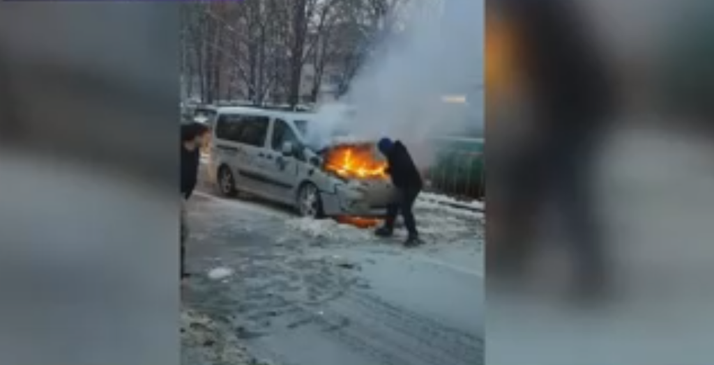 mașină în flăcări în plină stradă. focul, stins cu zăpadă de trecători