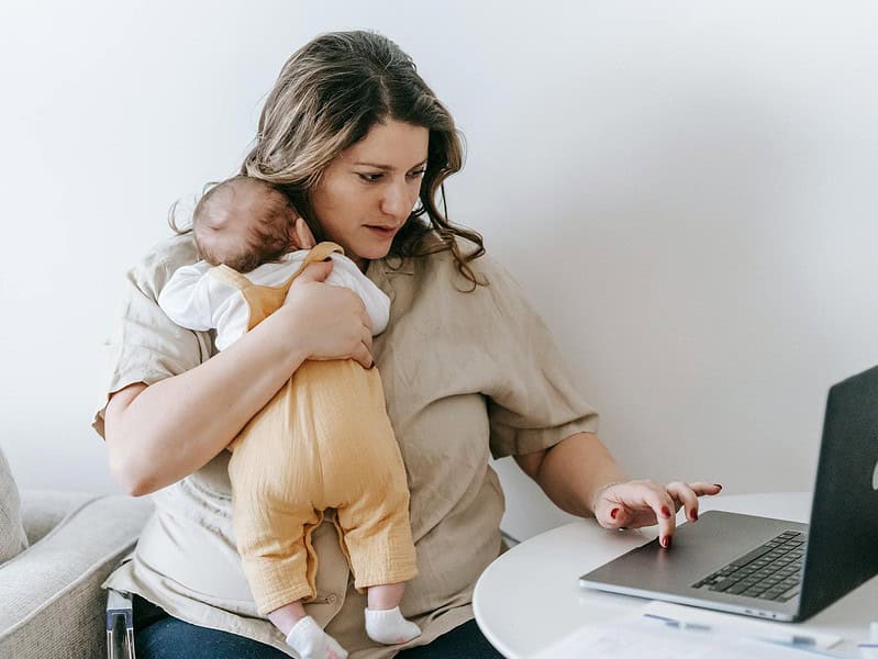 young working mother cuddling baby and using laptop at home