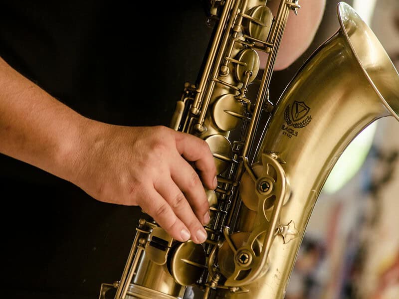 person in black shirt playing brass colored saxophone